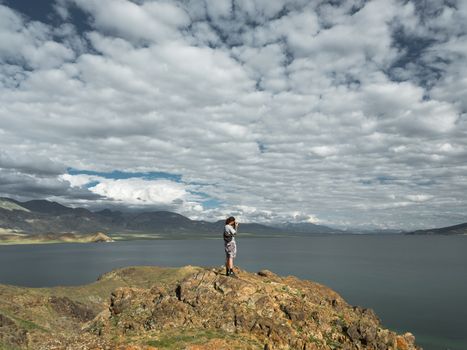 Man standing on a cliff taking a photo of a scenic ocean view in summer.
