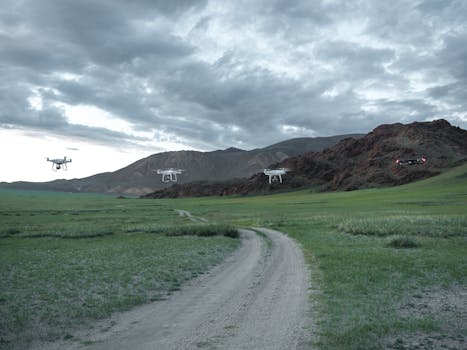 Aerial drones maneuver over a green field with dramatic clouds and rugged mountains in the background.