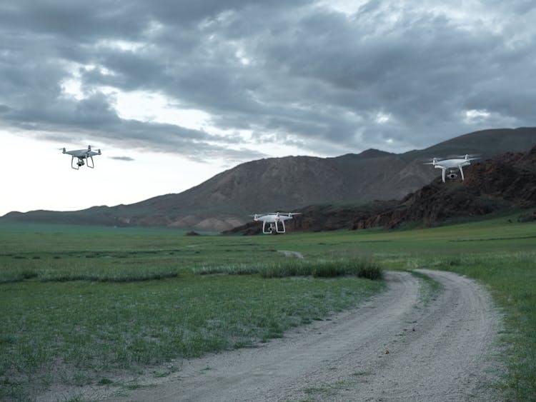 Drones Flying Along Field Road In Mountains