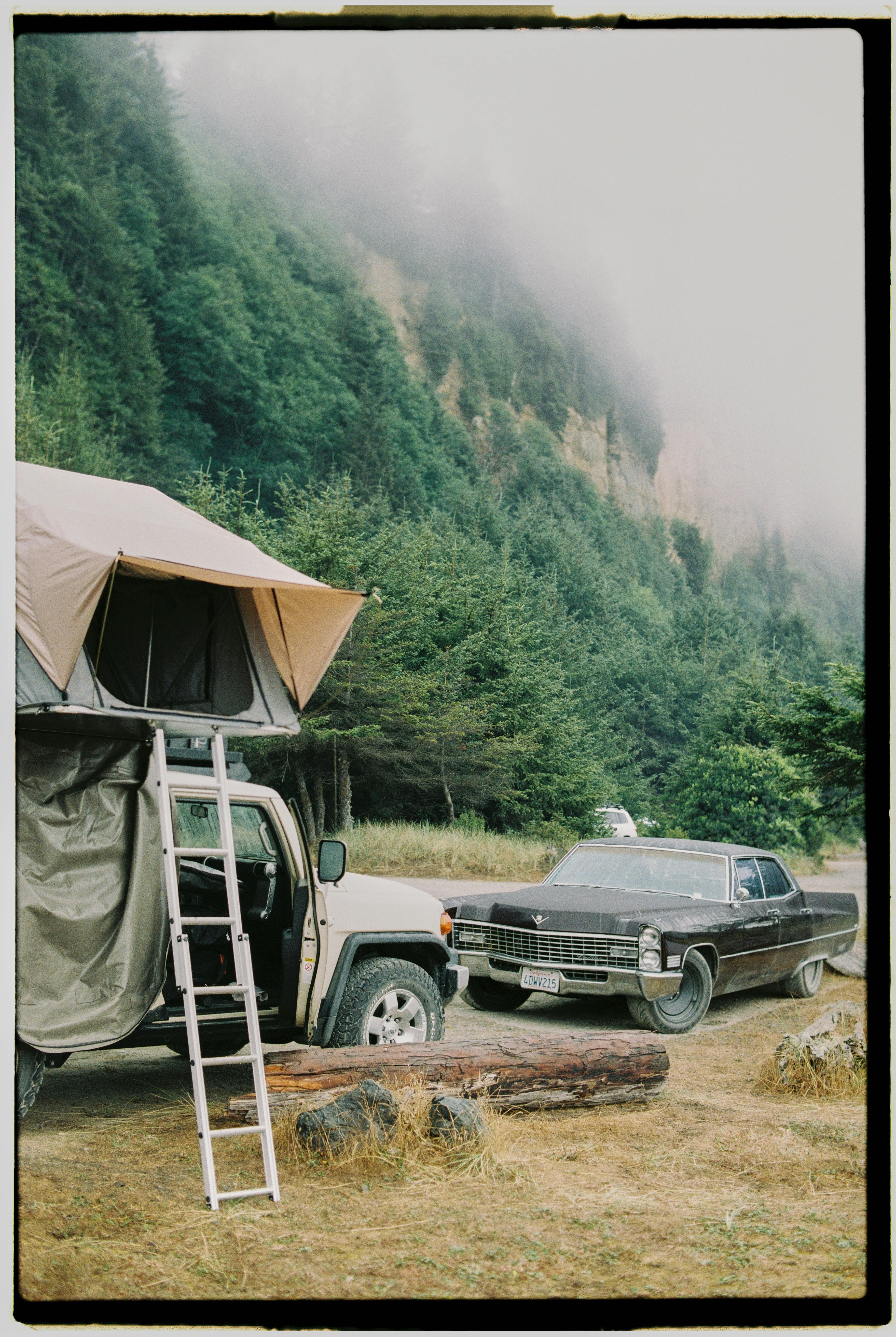 Jeep with rooftop tent and vintage car in misty forest campsite. Tranquil outdoor adventure.