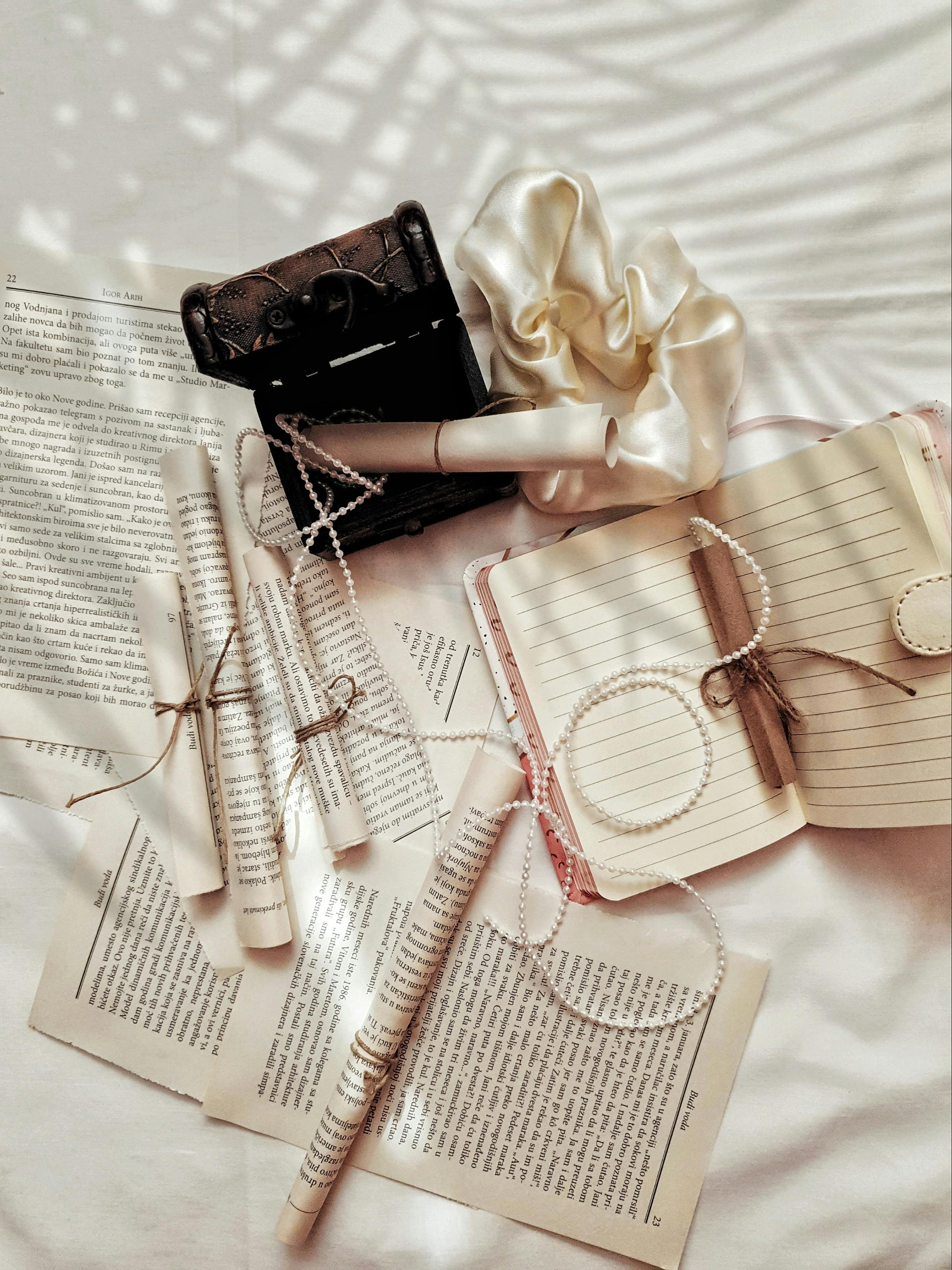 Aesthetic flat lay of vintage rolls, journals, and pearls with shadows on a white background.