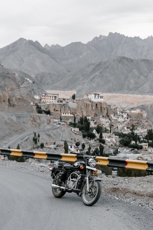 Free Motorcycle parked on a mountain road overlooking a remote village in the valley. Stock Photo