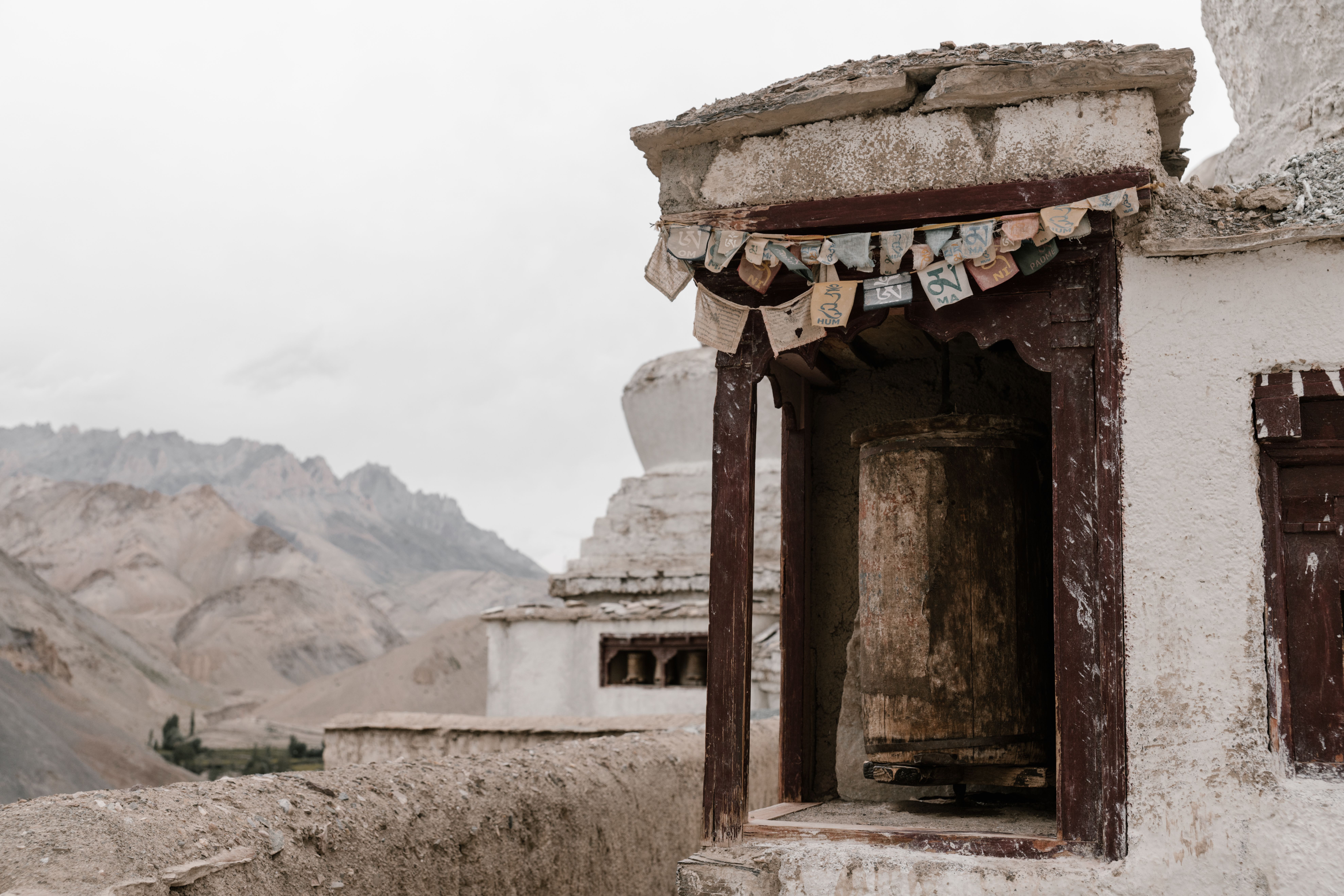 A rustic prayer wheel in a Tibetan monastery amidst serene mountain scenery.