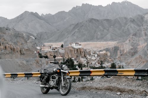 Free A classic motorcycle parked on a mountain road with a scenic view of a hillside village. Stock Photo
