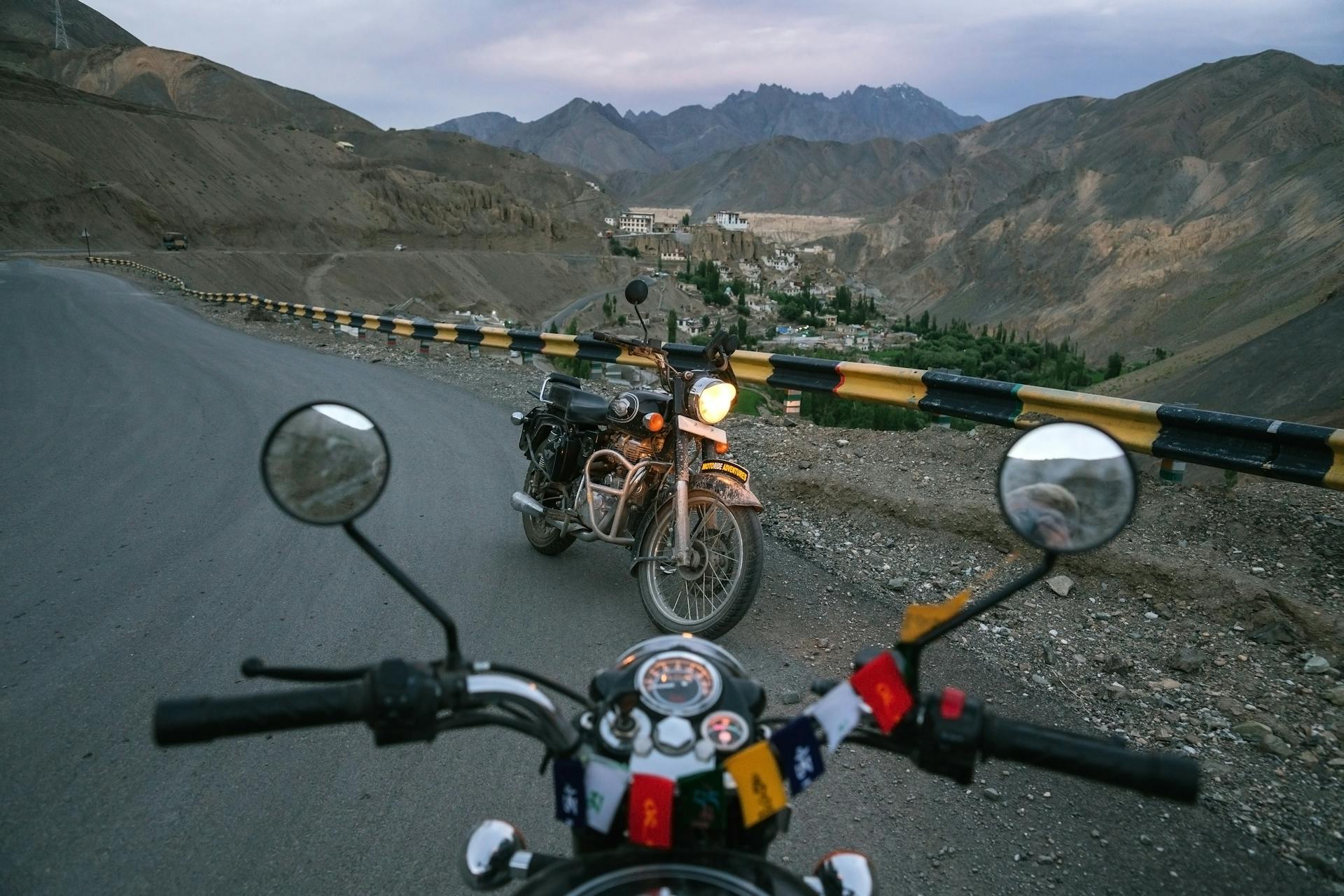 Two motorbikes on a winding mountain road with scenic valley view at dusk.