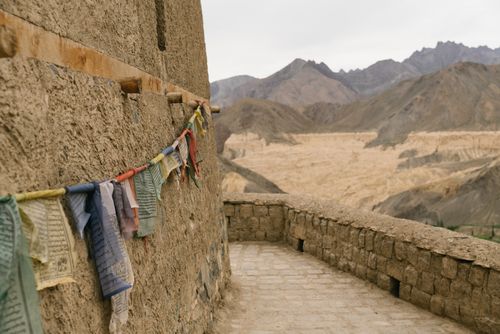 Free Colorful prayer flags hanging on a rustic wall with mountain backdrop, creating a spiritual scene. Stock Photo