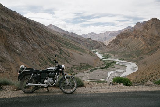 A motorcycle parked along a scenic road with a river winding through mountainous terrain, perfect for adventure trips.
