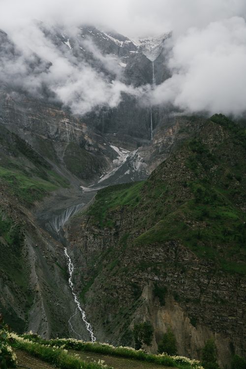 Free A stunning view of fog-covered mountains and a cascading waterfall in a lush green valley. Stock Photo
