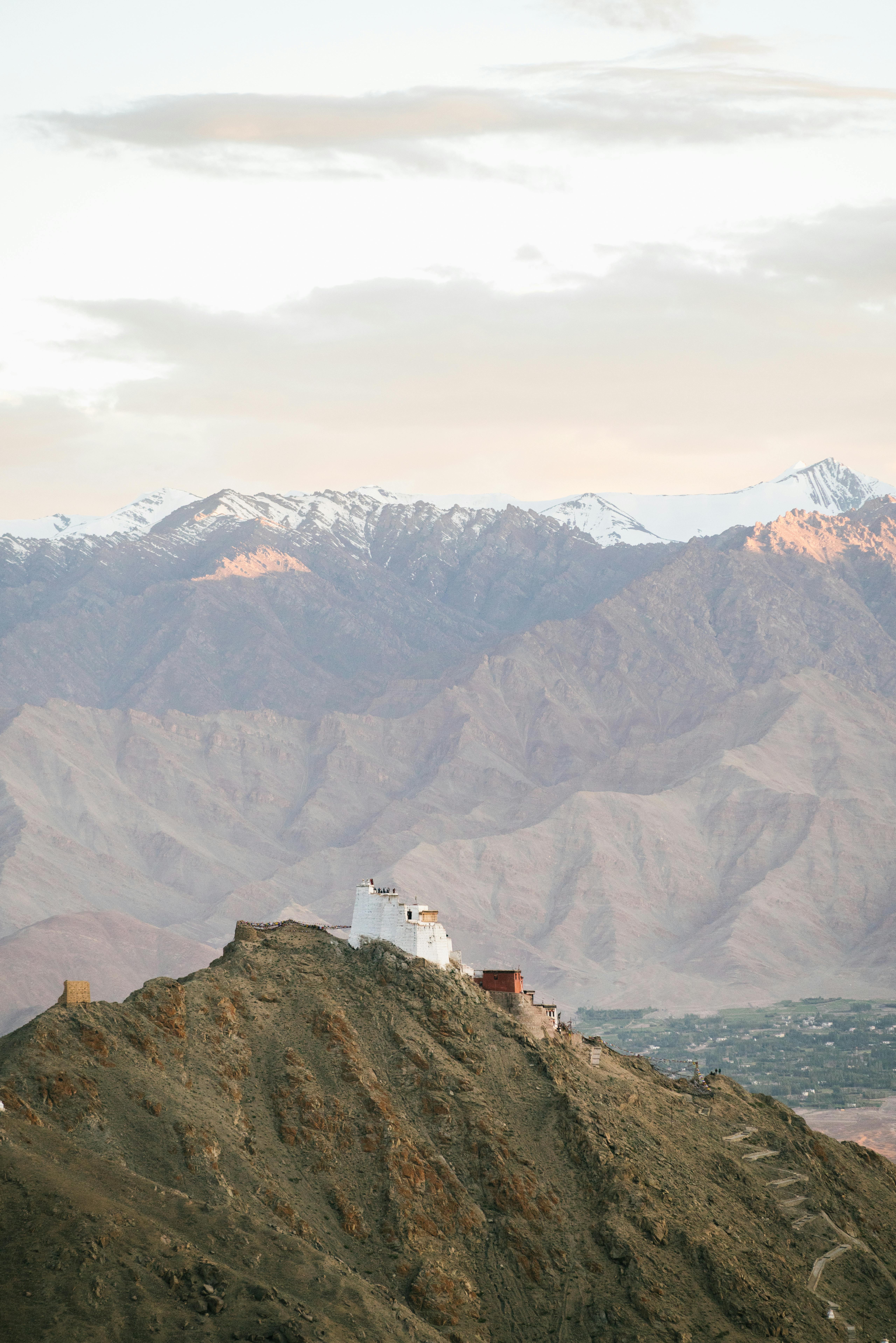 Dramatic landscape of a Tibetan monastery perched on a mountain with snowcapped peaks in the background.