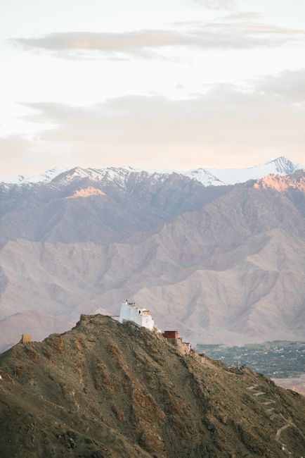 Dramatic landscape of a Tibetan monastery perched on a mountain with snowcapped peaks in the background.