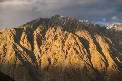 Free Dramatic sunlight casts golden hues on a rugged mountain landscape during sunset. Stock Photo