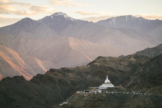 Breathtaking aerial view of Shanti Stupa in Leh, Ladakh with majestic mountains at sunset.