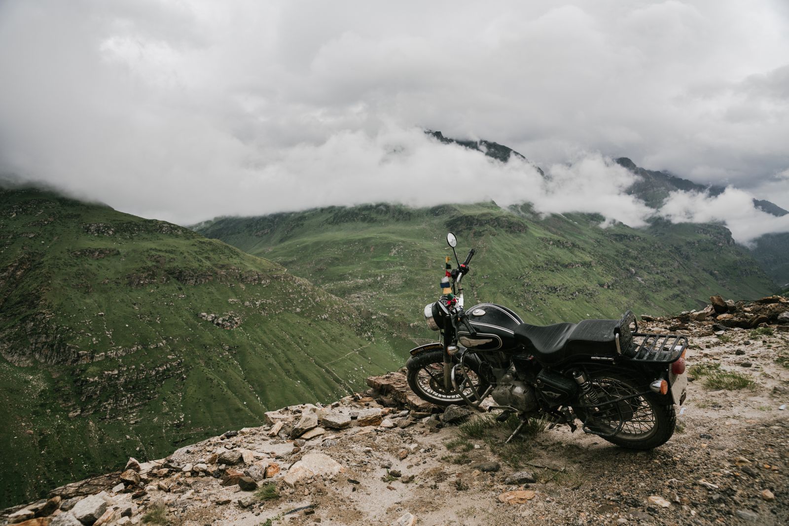 Moto garée sur une falaise rocheuse avec vue panoramique sur des montagnes verdoyantes