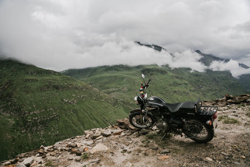 Moto garée sur une falaise rocheuse avec vue panoramique sur des montagnes verdoyantes