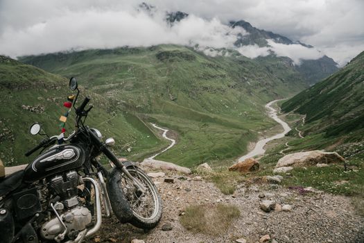 Motorcycle parked on a cliff offers a breathtaking view of green valleys and mountains.