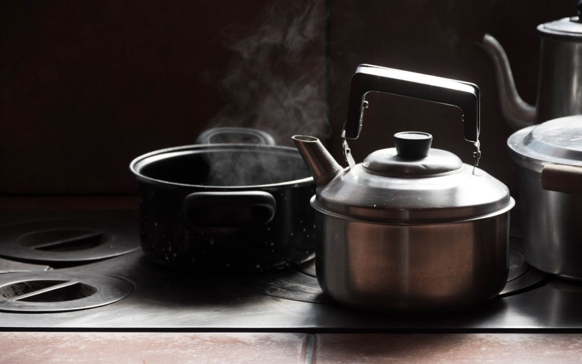 A steaming metal kettle and pot on a kitchen stove, emitting vapor.