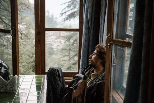 Free A man gazes outside a window on a rainy day, surrounded by nature. Stock Photo
