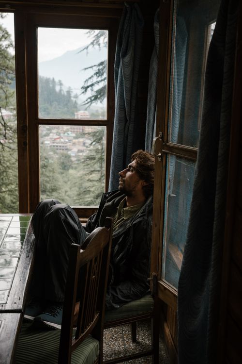 Free Pensive man sitting by a window in a wooden cabin, surrounded by mountains. Stock Photo