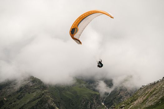 Experience the thrill of paragliding amidst lush mountain valleys and clouds.