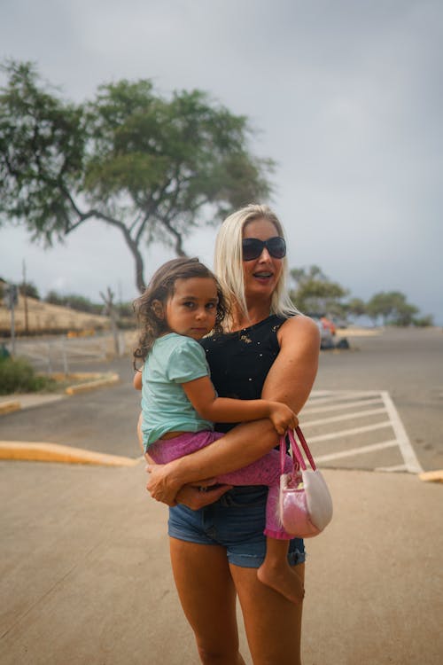 Free Cheerful joyful tanned blond carrying serious child on summer gloomy nasty cloudy day Stock Photo