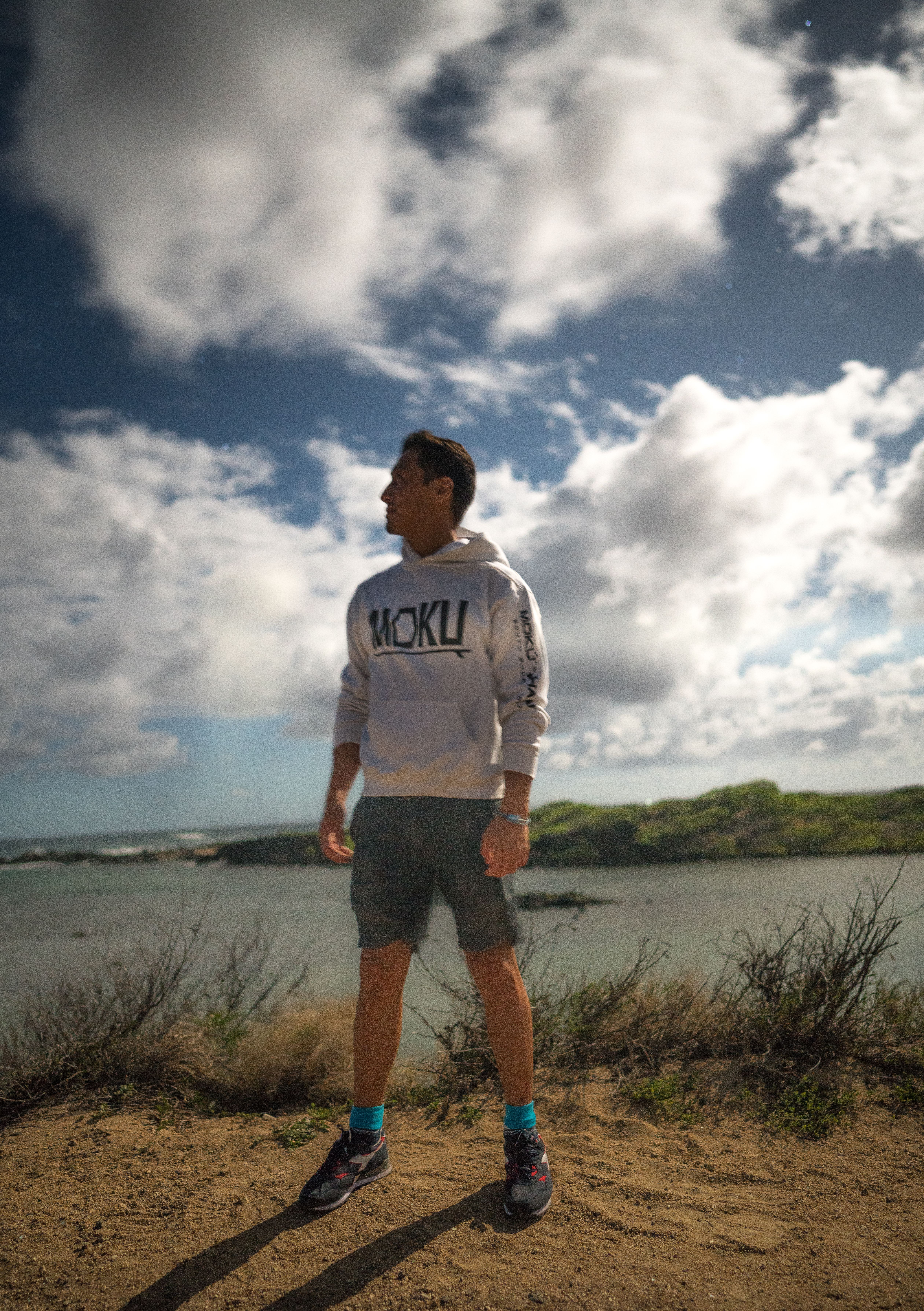 Full body of focused male in summer outfit looking away on sunny bank of river with green hills