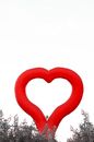 Red heart shaped balloon figure located above top of forest trees in gloomy weather
