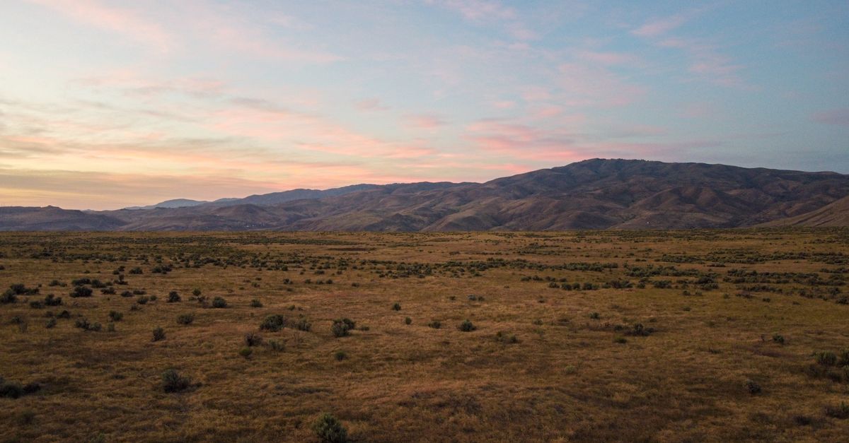 Picturesque view of dry grassy field near mountain ridge located under evening sky in summer day