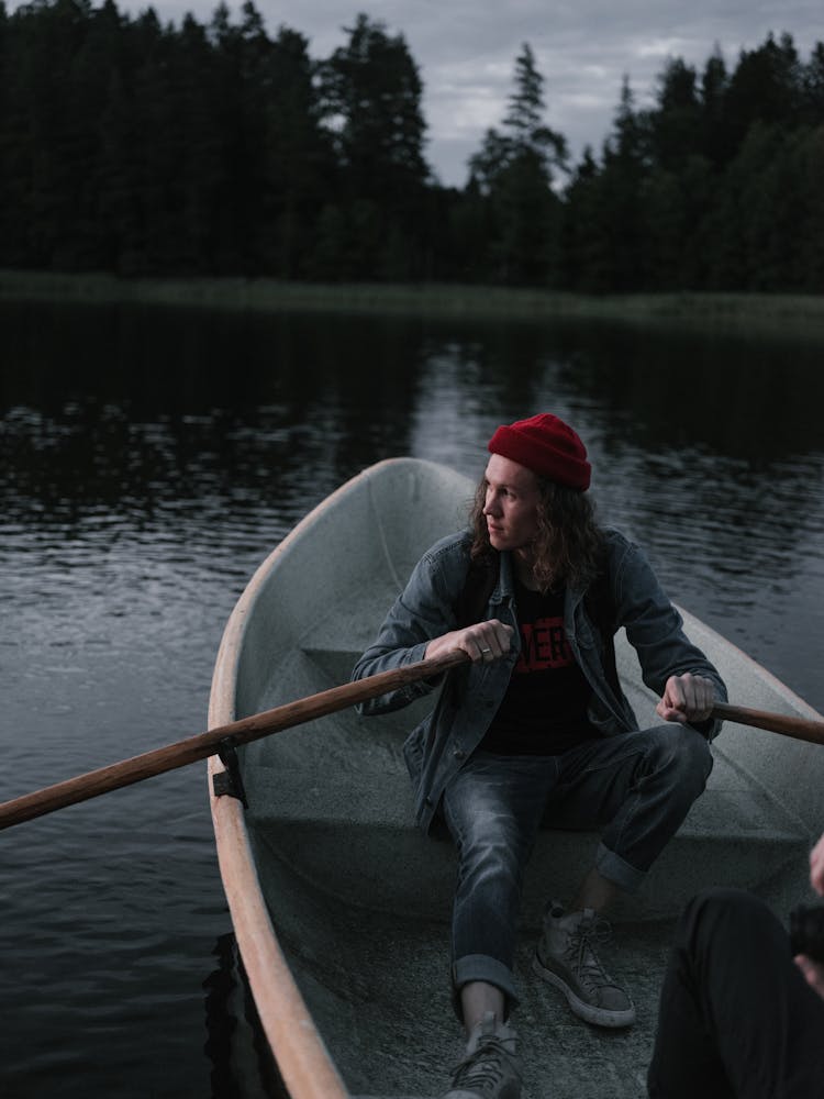 A Man Wearing A Red Beanie Sitting On A Wooden Boat