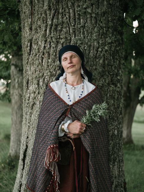 Woman in traditional attire meditates by a tree, embracing nature's serenity.