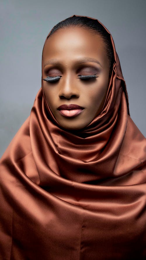 Young stylish African American female in satin headscarf and bright lipstick on gray background