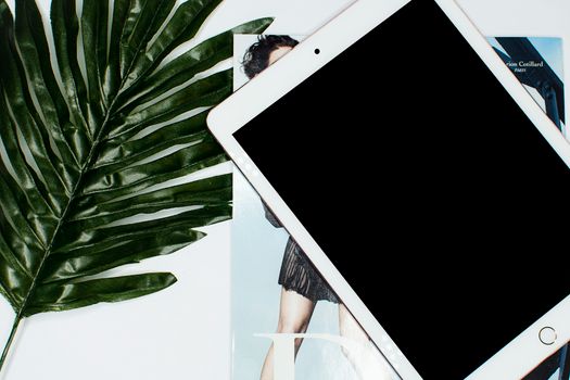 A tablet placed on a magazine with a large green leaf, perfect for tech and lifestyle concepts.