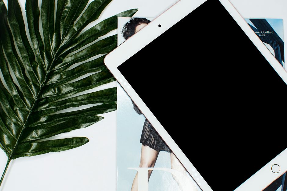 A tablet placed on a magazine with a large green leaf, perfect for tech and lifestyle concepts.