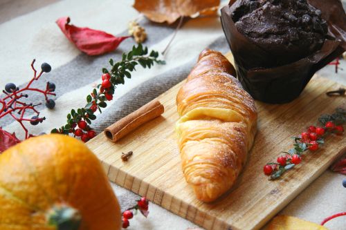 Free Close-up of a croissant and chocolate muffin on a wooden board with fall decorations. Stock Photo