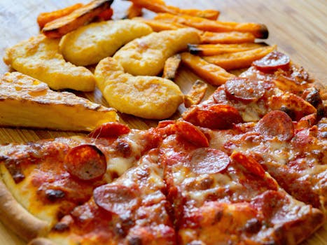 Close-up of diverse fast food including pizza slices, sweet potato fries, and chicken nuggets.