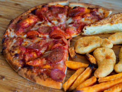 Close-up of pepperoni pizza, battered chicken, and sweet potato fries on a wooden surface.