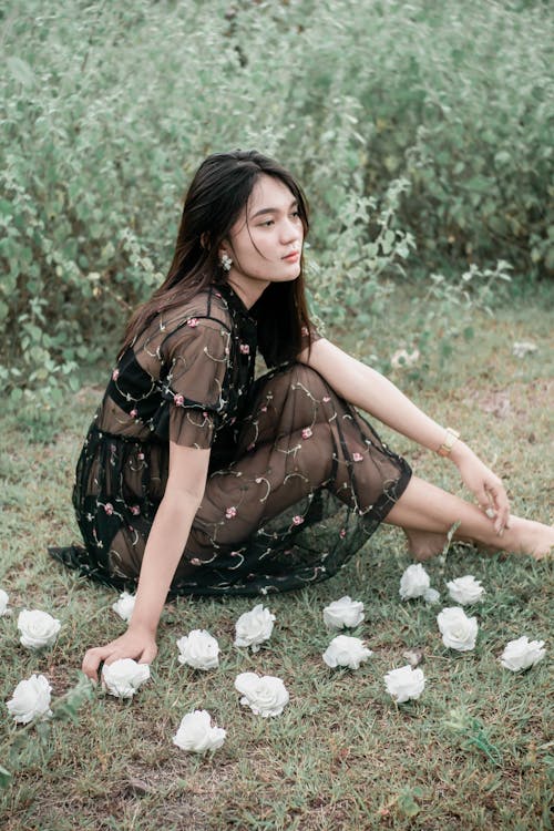 From above side view of young peaceful female in black transparent dress resting in green meadow in countryside