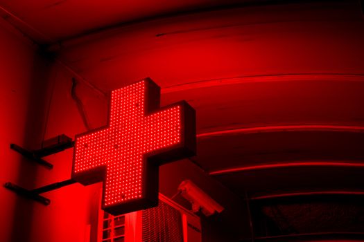 A vibrant red cross sign glowing brightly in a nighttime urban setting.