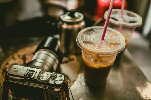 A close-up view of iced coffee cups with straws next to a vintage camera on a table.