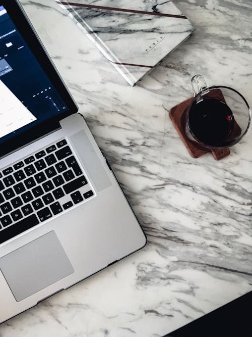 Free From above of opened laptop and notebook and cup of coffee placed on white marble table Stock Photo