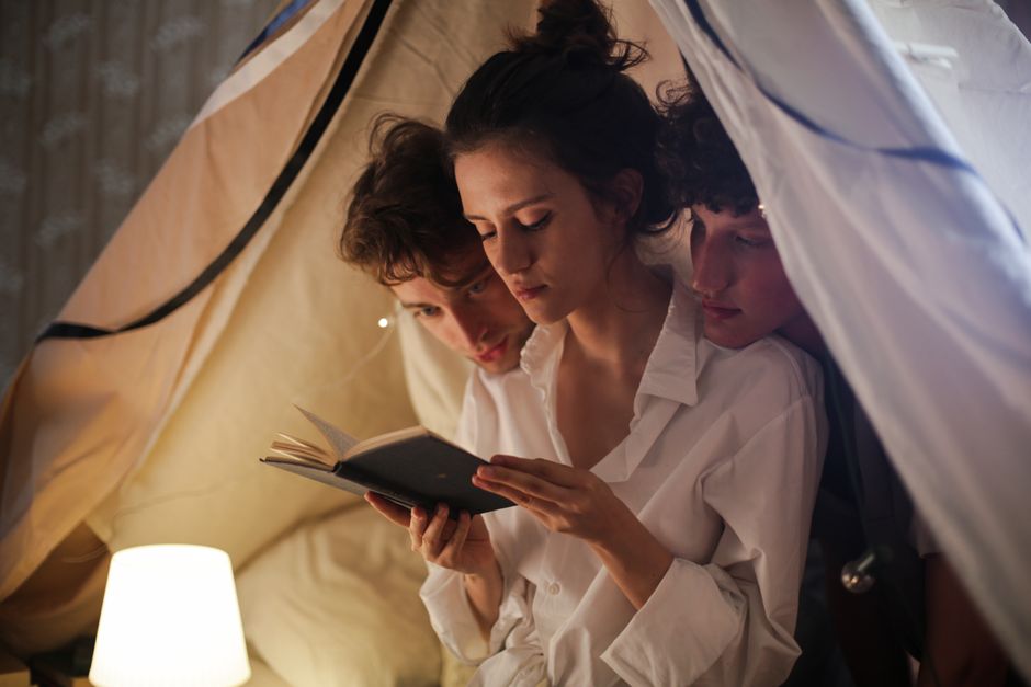 세 친구가 아늑한 실내 텐트에서 부드러운 조명 아래 편안한 독서 시간을 즐기고 있습니다.