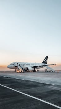 A passenger airplane parked on an airport tarmac at sunset, with clear skies.