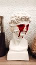 Decorative bust sculpture with bandaged eyes and flowing bloodshot on wooden surface against white wall