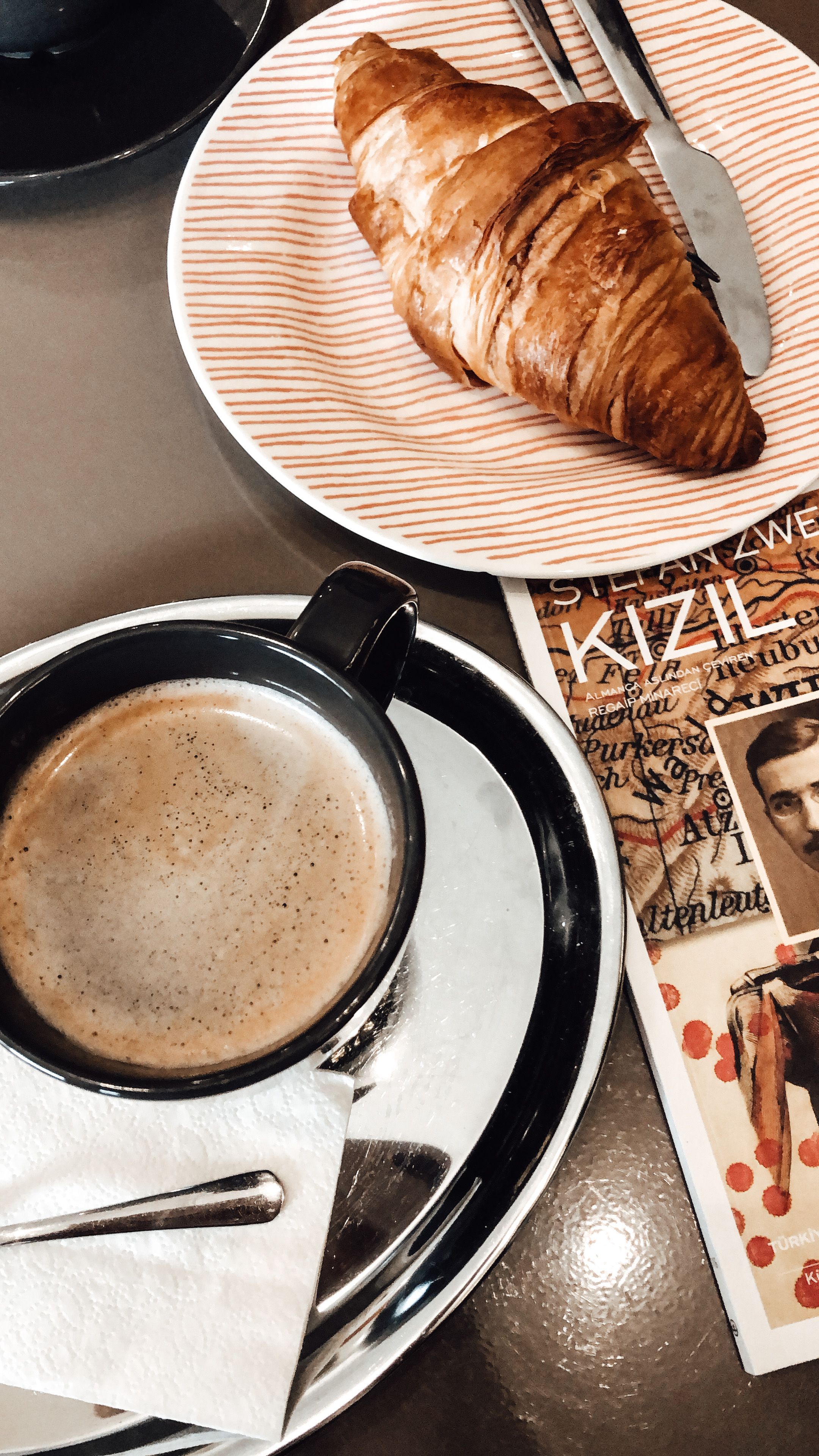 From above of cup of aromatic coffee and fresh croissant placed on table in cafe at daytime