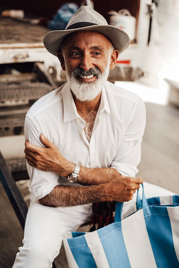 Smiling Senior Man With Tote Bag Sitting On Street