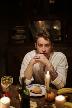 一个男人坐在烛光餐桌旁，周围是食物和温暖的气氛，他正沉思着