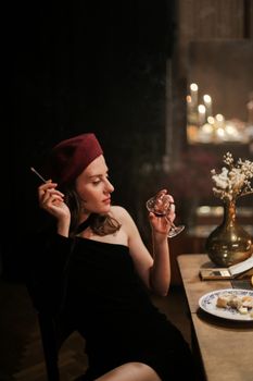 一位时尚女子戴着贝雷帽，在烛光晚餐上享用葡萄酒和香烟