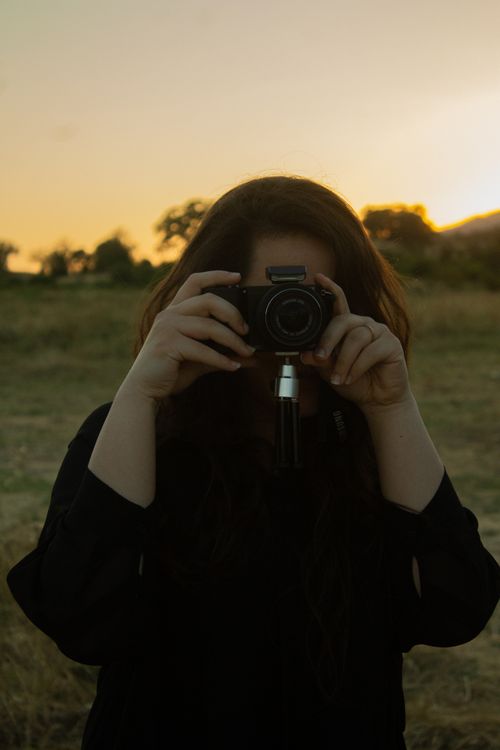 Free Unrecognizable woman taking a photo in the countryside during sunset. Stock Photo