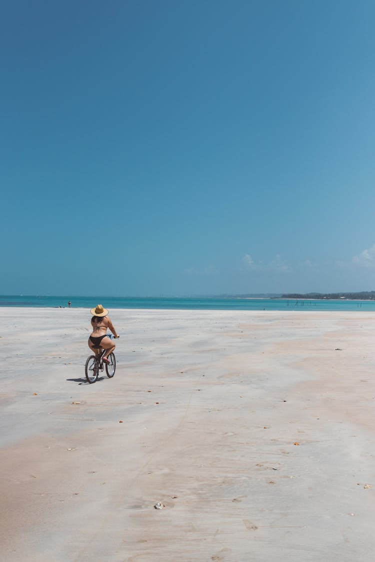 A Woman In A Bikini Riding A Bicycle On The Beach