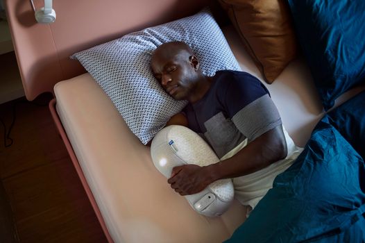 成年男子在舒适的卧室环境中与睡眠机器人一起睡觉，以增强身心放松