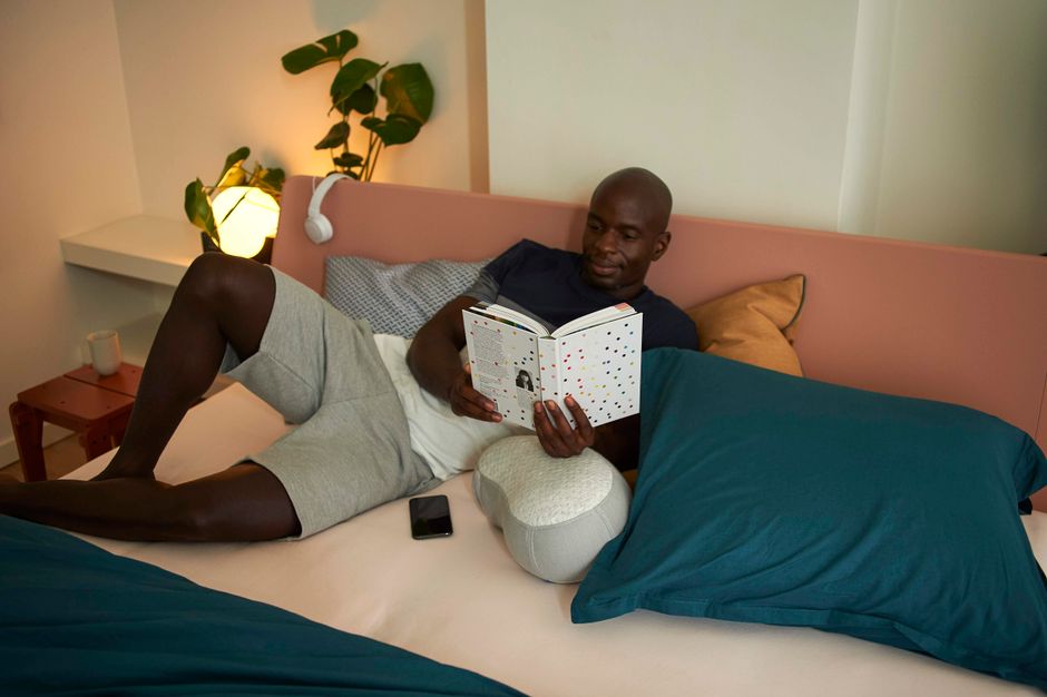 Man relaxing and reading a book in a cozy, modern bedroom with ambient lighting.